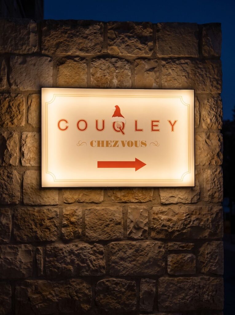 Illuminated Couqley directional sign mounted on a stone wall.