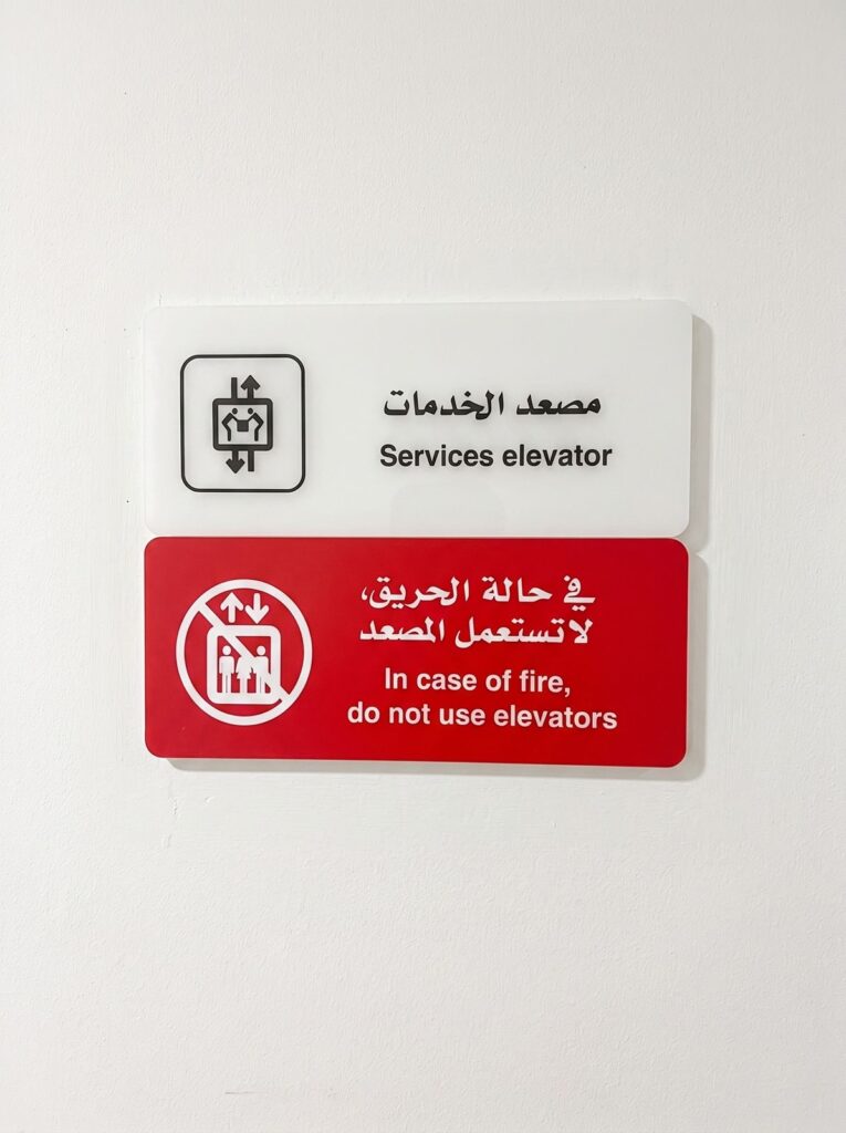 Arabic and English service-elevator and fire-warning signs mounted on a wall.